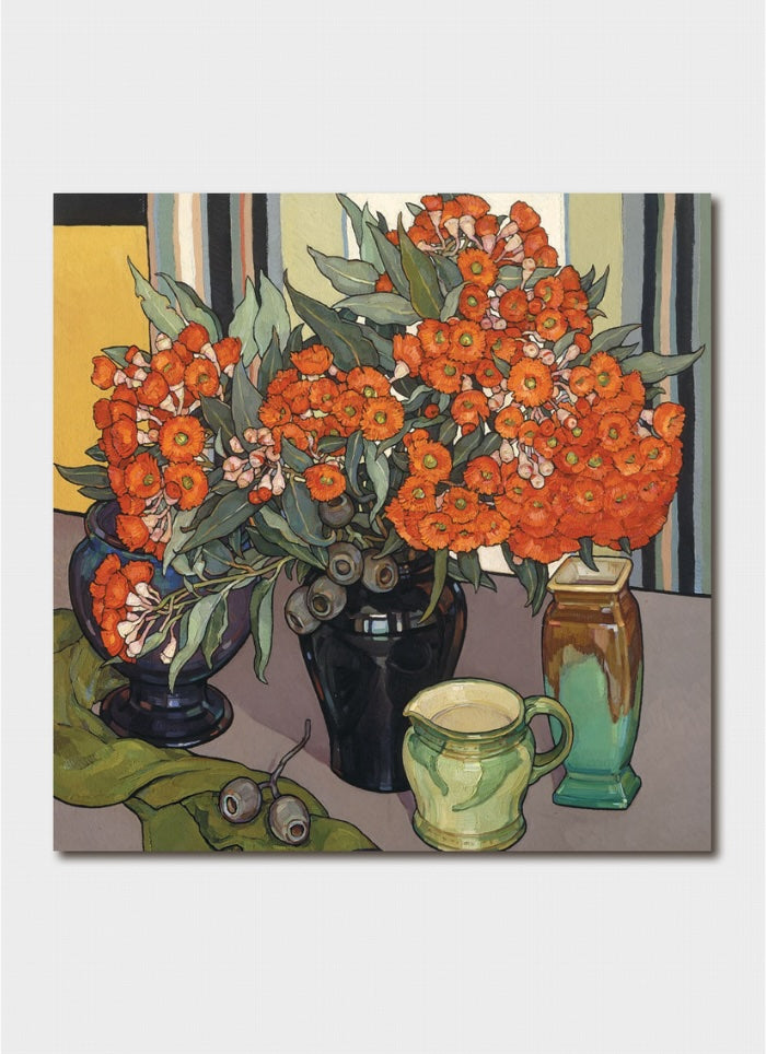 Red flowers in a black vase on a table with another vase, a jug and some seed pods.