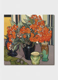 Red flowers in a black vase on a table with another vase, a jug and some seed pods.