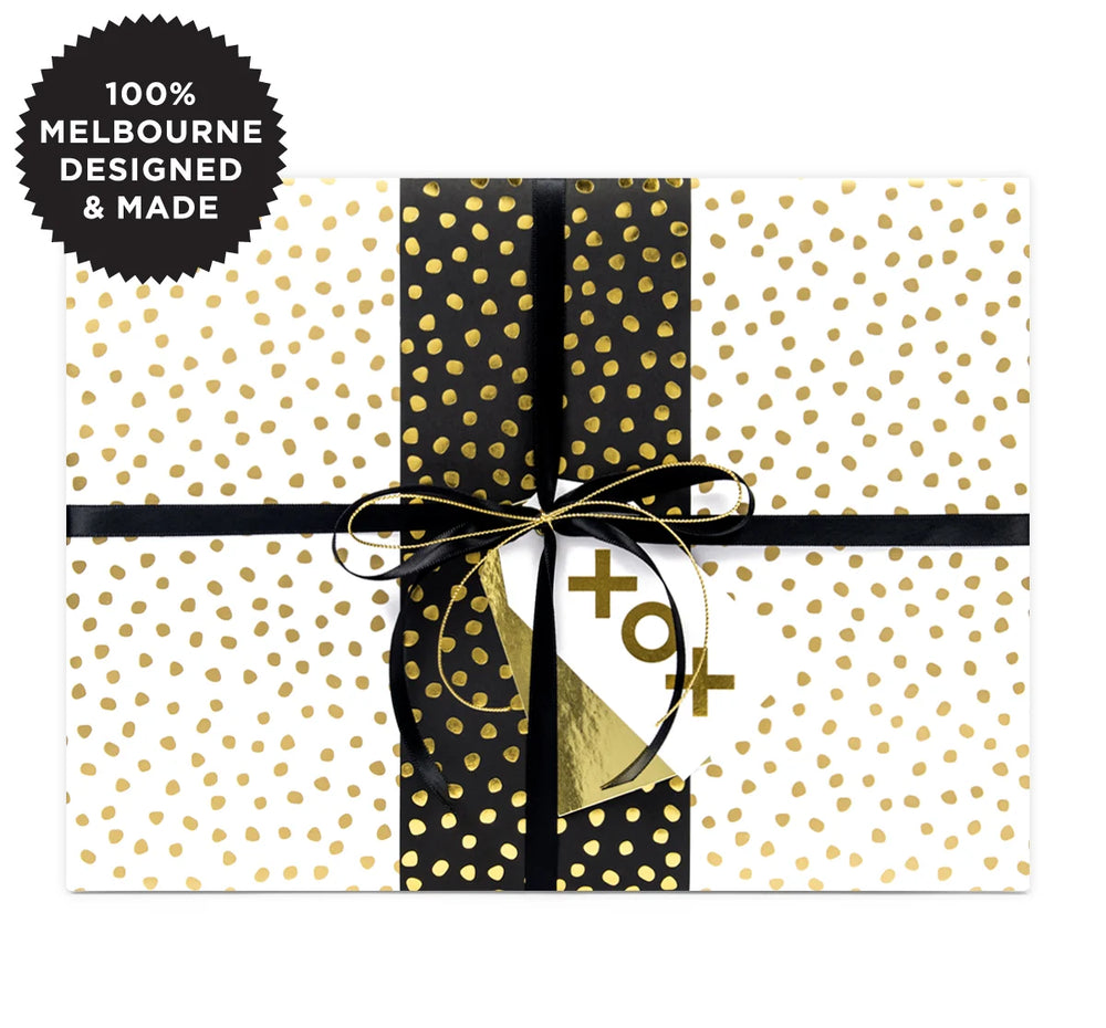 A gift wrapped with white paper with gold spots and black and gold ribbon.
