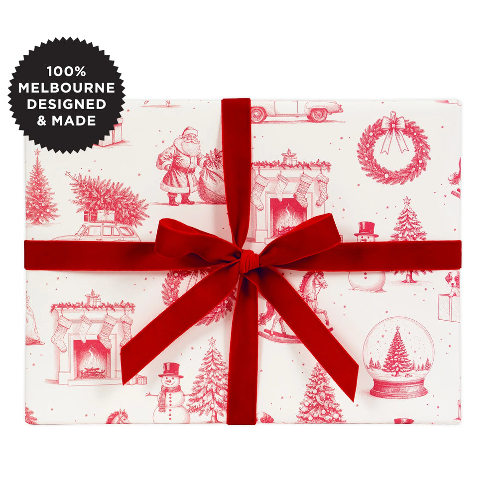 A gift wrapped in pink on white Christmas themed paper with a red velvet ribbon.
