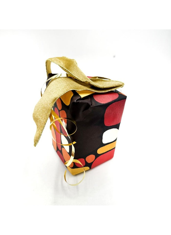 A small gift box wrapped in black paper with a bold red, orange, and white abstract pattern, tied with a shiny gold ribbon and bow on a white background.
