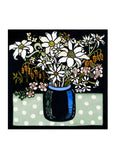 A square card with a vase of flannel flowers and other natives in a blue vase on a green and white spotted tablecloth