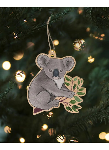 Decorative koala ornament hanging on a Christmas tree with lights in the background