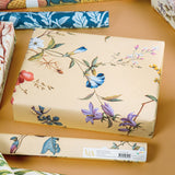 Floral-patterned gift box on a wooden surface with additional wrapping paper in the background.