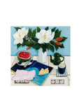 White vase with white flowers on a table with an open book, fruit, cup and coffee pot.
