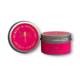 Two round metal tins for candles on a white background. One tin is open, showing a bright pink lid with gold lettering that reads 'MURPHY & DAUGHTERS SECRET GARDEN' and a gold dragonfly.