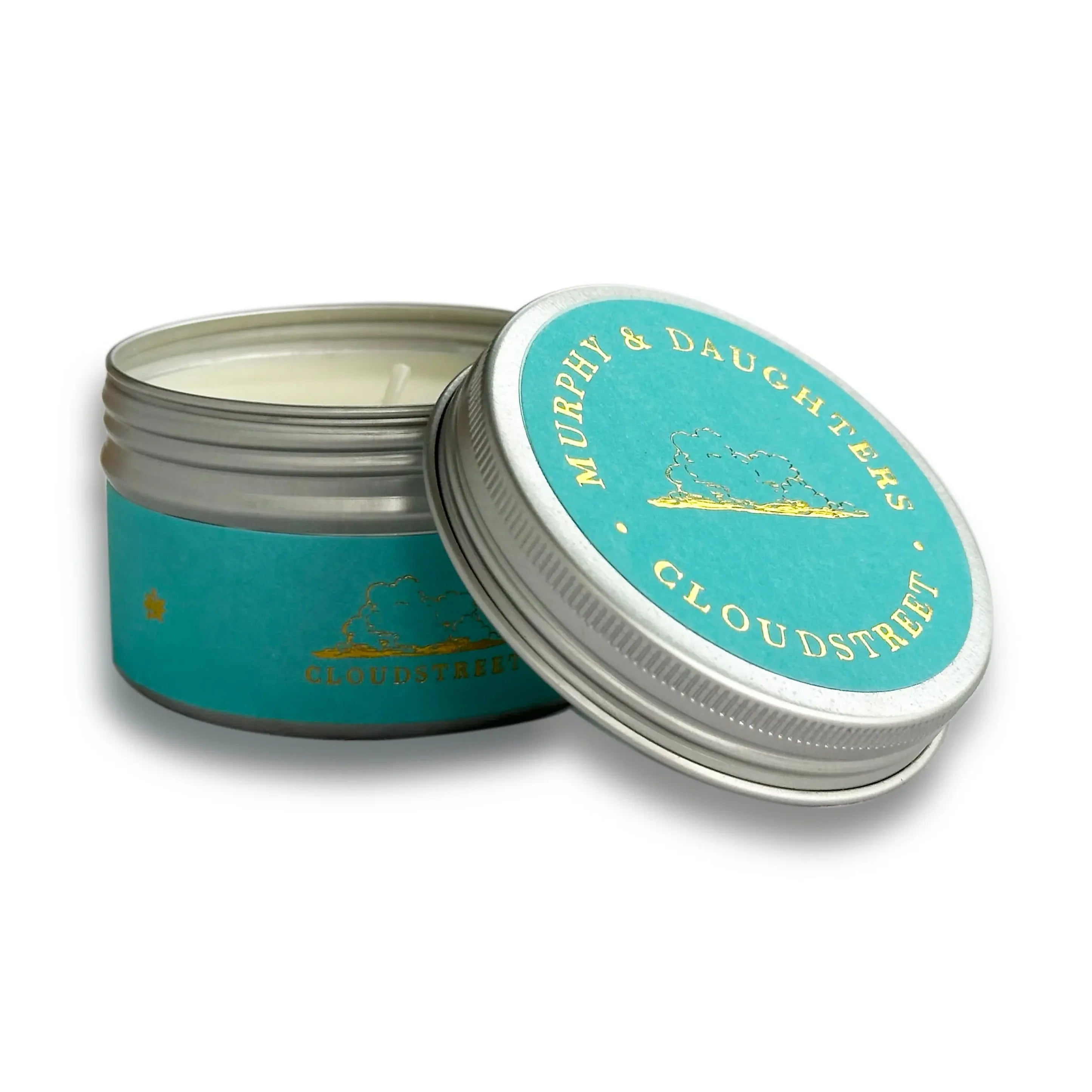 An open round metal tin candle with a turquoise label and silver lid, shown on a white background. The label reads 'MURPHY & DAUGHTERS CLOUDSTREET' with a small gold mountain illustration.