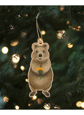 Bear-shaped ornament hanging on a Christmas tree with lights in the background