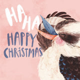 A festive Christmas illustration featuring a close-up of a kookaburra with a blue beak and black-and-white feathers against a soft pink background, with the text 'HA HA HAPPY CHRISTMAS' in white and blue lettering.