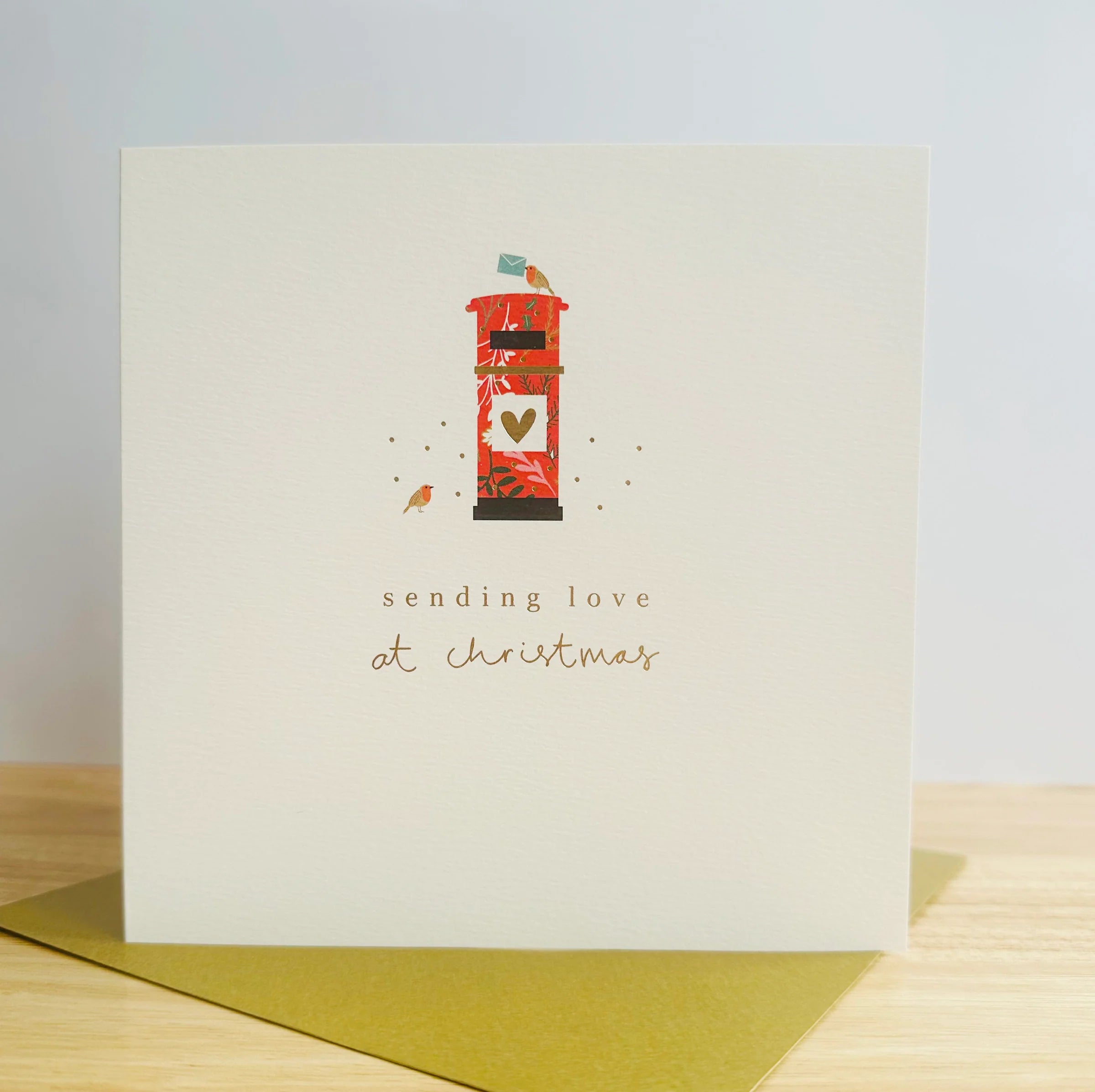 A cream card with a red postbox with a gold heart on it and the words sending Love at Christmas