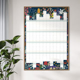 A framed 2026 wall calendar hanging on a light gray wall, styled next to a green potted plant. The calendar features a colorful floral border and illustrated monthly grids.