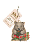 Wooden decoration of a wombat holding flowers with 'earth greetings' tag on a white background
