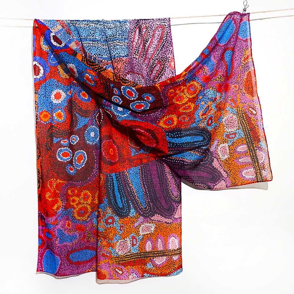 A lightweight sheer scarf with a vibrant, multicolored Aboriginal dot-art pattern, draped over a white line against a plain white background.