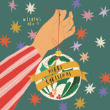 Illustration of a hand holding a Christmas ornament with 'Merry Christmas' text against a colorful star-patterned background.