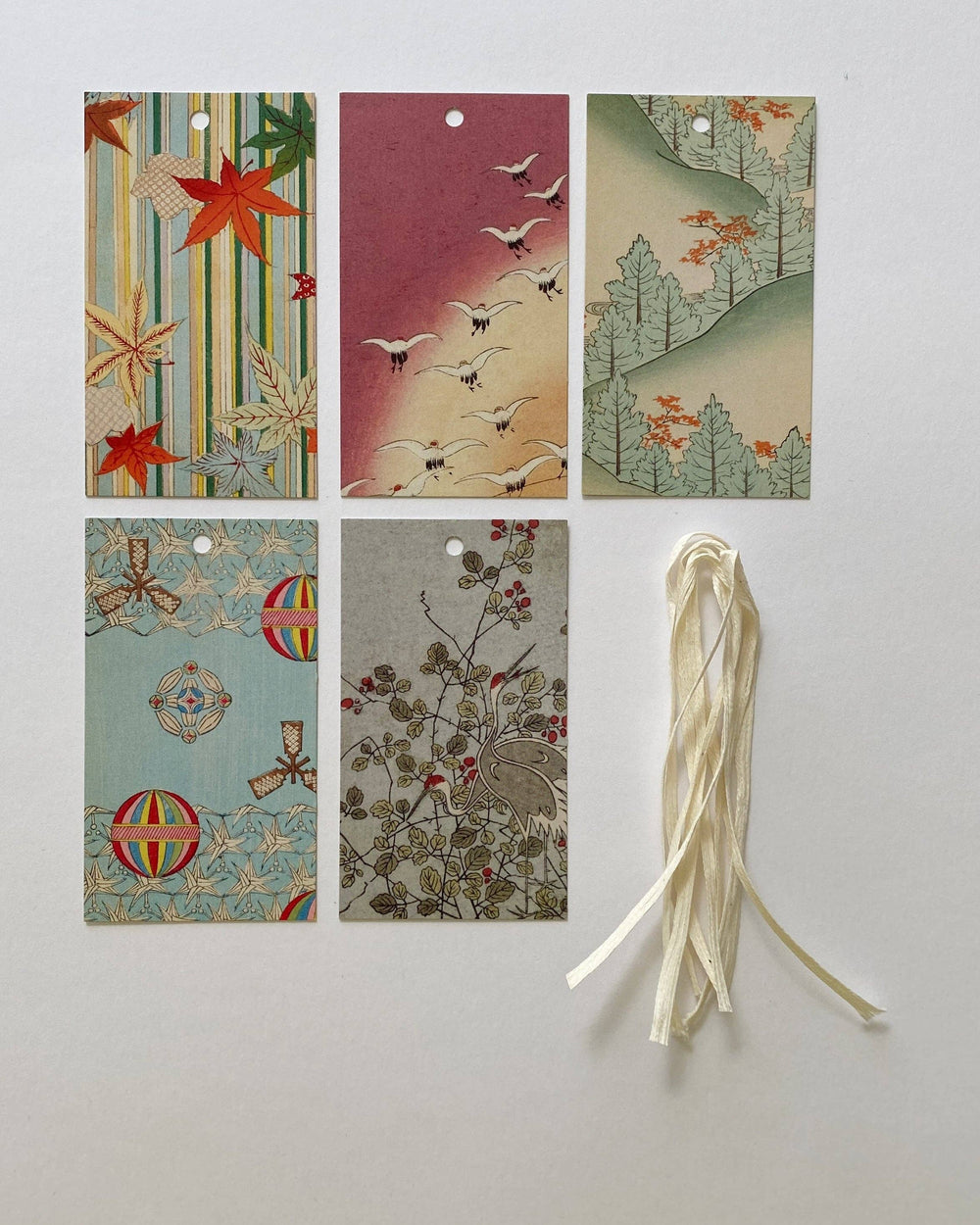 Six decorative paper tags with Japanese-inspired patterns and illustrations, arranged on a light gray background next to a cream-colored ribbon.