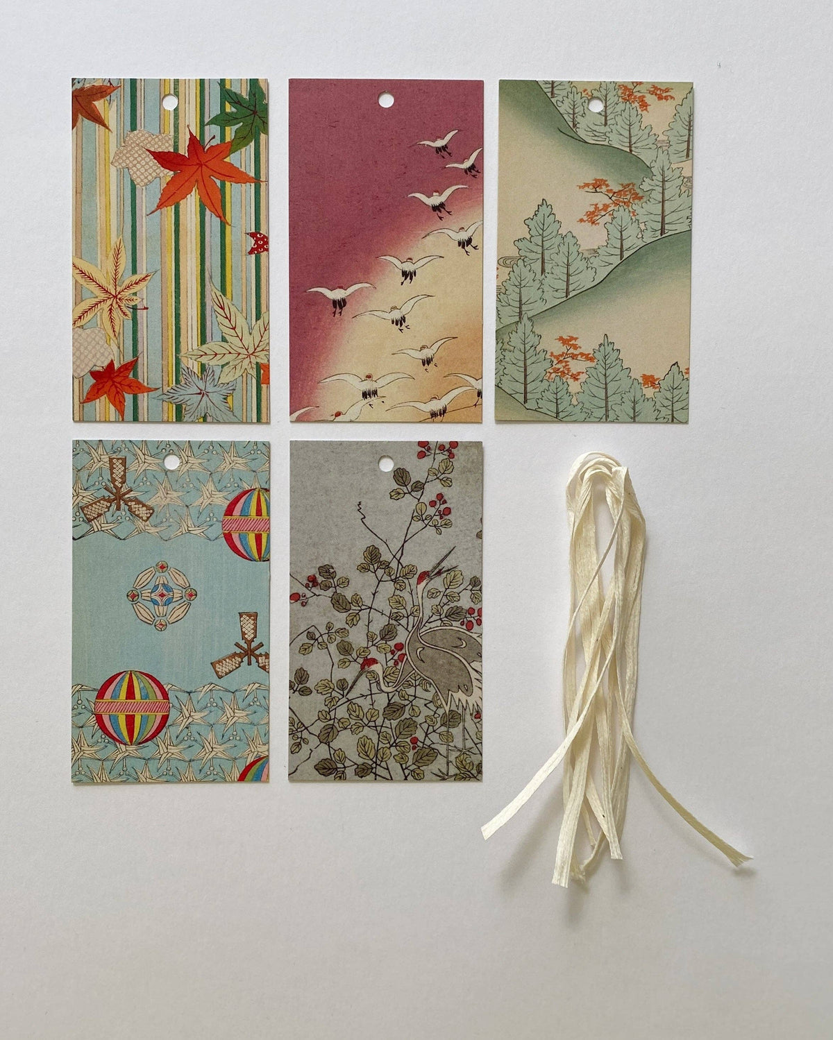 Six decorative paper tags with Japanese-inspired patterns and illustrations, arranged on a light gray background next to a cream-colored ribbon.