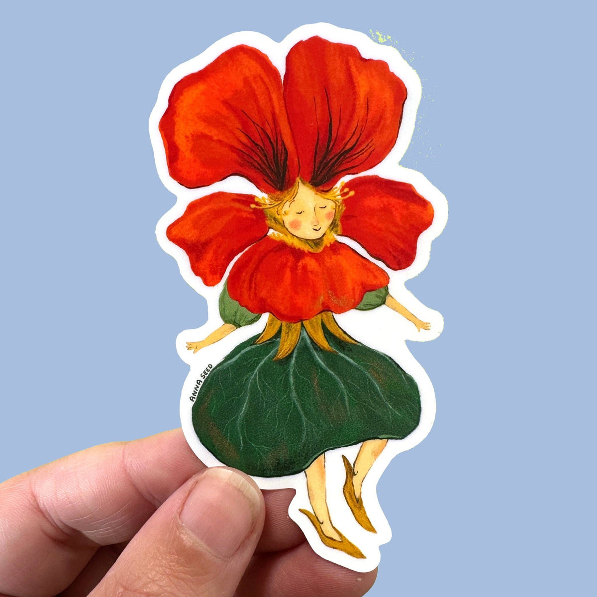 A die-cut sticker featuring a whimsical fairy-like figure with a large red flower head, gold hair, and a green leaf skirt, held by a hand against a light blue background.